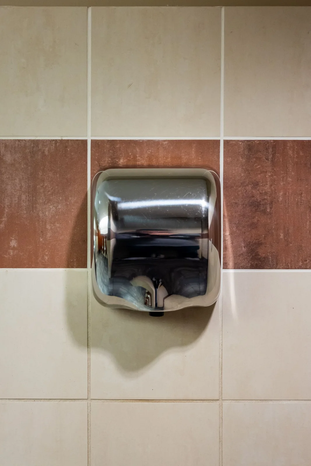 Stainless steel hand dryer on a clean tiled restroom wall